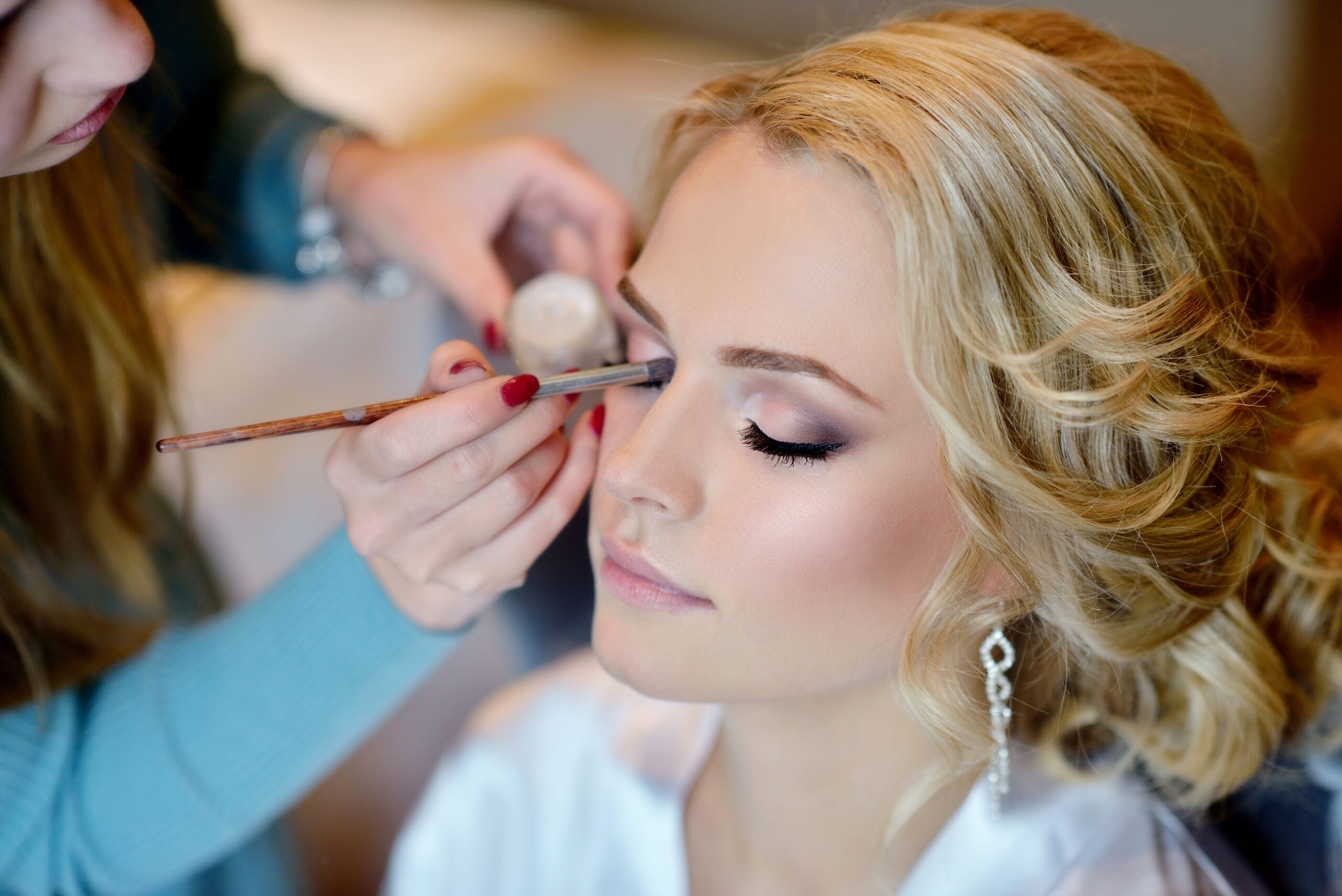 Wedding makeup artist making a make up for bride. Beautiful sexy model girl indoors. Beauty woman with curly hair. Female portrait. Bridal morning of a cute lady. Close-up hands near face